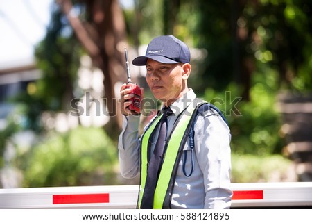 Portrait Of Asian Male Security Guard Talking a portable wireless transceiver entrance the village on a blurry background,use a filter