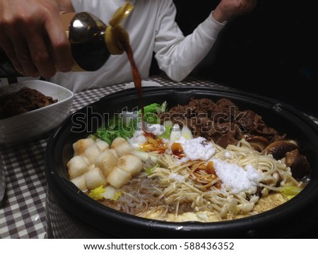 Man pouring soy sauce over vegetables, seafood and meat in casserole of Sukiyaki dinner, Kansai-style. Royalty-Free Stock Photo #588436352