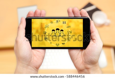 Watching two hand holding mobile phone with digital advertise marketing features on screen and blur desk office background,Digital content concept