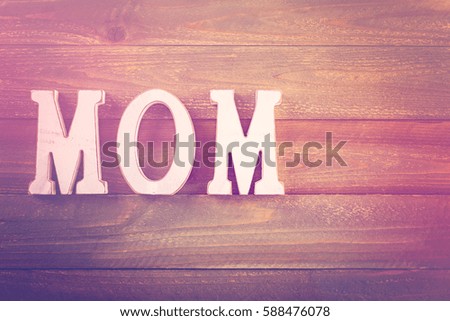 White letters MOM on a painted wood background.