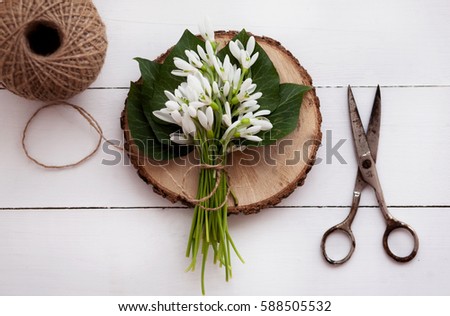 on a wooden white table, bouquet of snowdrops, thread and scissors. Spring decoration