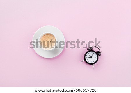 Morning cup of coffee and alarm clock on pink working desk top view in flat lay style.