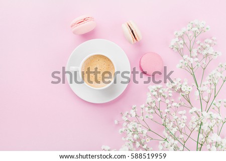 Morning cup of coffee, cake macaron and flowers on pink table top view in flat lay style. Beautiful breakfast for woman