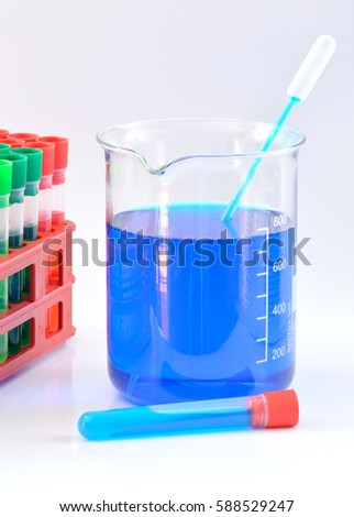 Glass chemical beaker with blue chemicals dissolved in water, laboraty pipette and tube, set of chemical tubes in background
