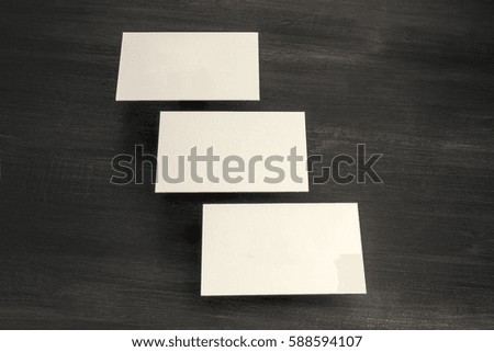 A photo of blank white thick cardboard business cards, floating above a dark wooden background texture. A mockup or a minimalist banner with copy space