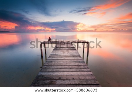 Sunset over a wooden jetty with reflection. Image may contain soft focus and blur due to long exposure.