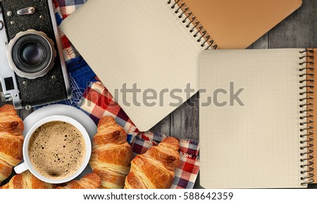 Coffee with foam and croissants on a wooden table. Notebook, old cameras, background.