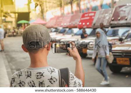 Young man take a photo of his sister by mobile which she stand at front of many car
