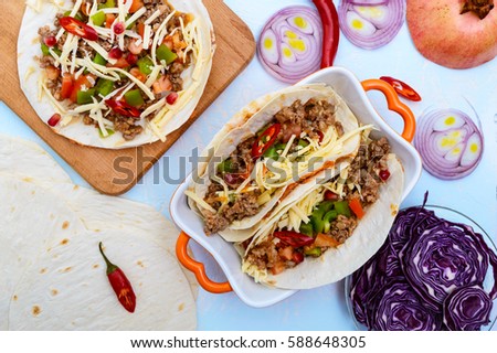 Spicy Mexican tacos with minced meat, mashed beans, vegetables, grated cheese. The top view.