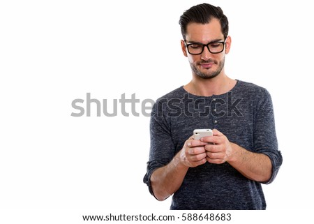 Studio shot of young handsome man using mobile phone while wearing eyeglasses
