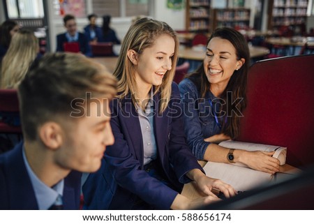 Teen student is working with her teacher on the computer during her lesson. They are talking and laughing.  Royalty-Free Stock Photo #588656174