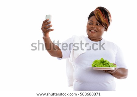 Happy fat black African woman smiling while taking selfie picture with mobile phone and holding lettuce served on white plate