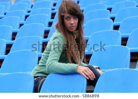 The girl sit on the blue plastic chairs in the stadium.