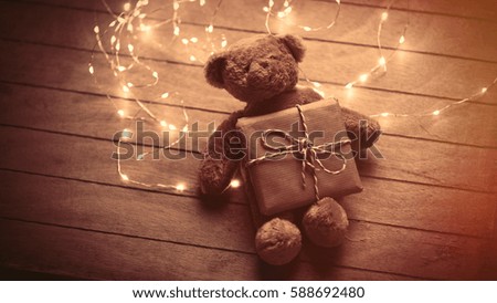 cute fluffy teddy bear with gift and bright garland on the wonderful brown wooden background