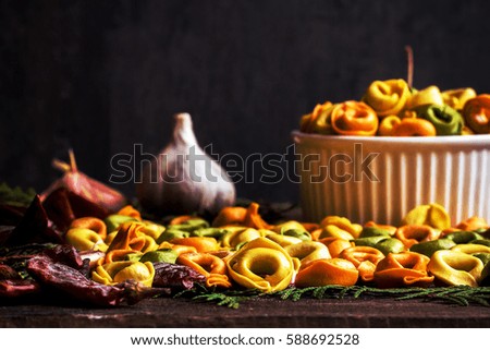Italian pasta tortellini with flour and pepper in white plate on black wooden background, front view place for text