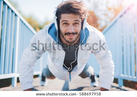 Young sportsman listening to music while doing push ups outdoors, fitness and exercising in the park. Fitness, sport, lifestyle concept Royalty-Free Stock Photo #588697958