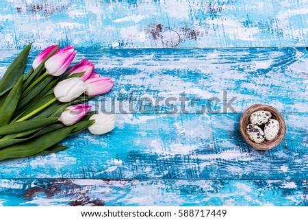 Easter eggs in nest and tulips on wooden background. Top view with copy space. Happy Easter card