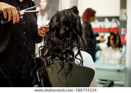Young woman getting her hair curled by a stylist at a beauty salon. Close up of stylist's hand using curling iron for hair curls Royalty-Free Stock Photo #588759224