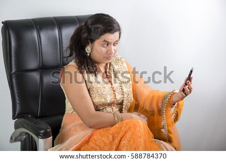 Happy traditional Indian businesswoman at office chair taking selfie with cell phone.