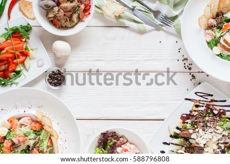 Warm salads frame on white wood flat lay. Top view on restaurant table with assortment of meat side dishes, free space. Buffet, banquet, menu concept Royalty-Free Stock Photo #588796808