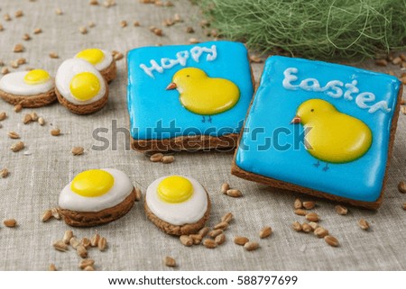 Square cakes with a picture of chickens on a blue background and the words Happy Easter are near gingerbread patterned eggs
