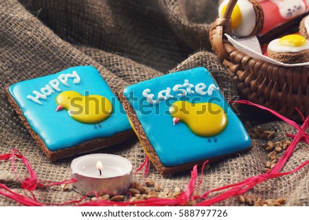 Square cakes with a picture of chicks and Happy Easter sign on a table covered with burlap close to wicker basket with gingerbread