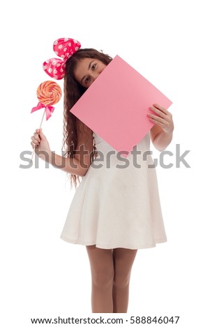 Lovely girl brunette with long hair in a white dress with a bow on her head with candy and a sheet of paper in the hands posing on a white background in studio
