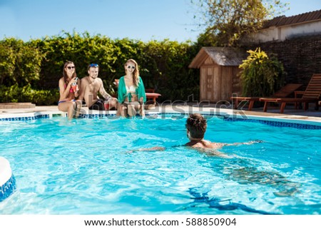Young cheerful friends smiling, laughing, relaxing, swimming in pool.