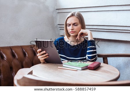 Young beautiful woman reading electronic book via internet on digital tablet while relaxing in cafe. Attractive female watching breaking news on touch pad while waiting order in cafe.