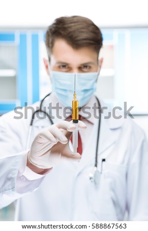 portrait of serious doctor in mask holding syringe in lab