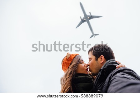 A guy and a girl, the couple embraced doing selfie standing in a picturesque place rocks. Against the background of a plane flies overhead. Autumn sky. Brunette long hair, knitted bandage