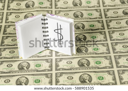 Sheet of dollar bills and a pad of paper with a money sign