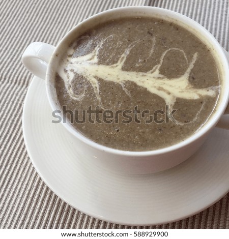 Mushroom soup with art cream picture on top in white bowl on white plate on fabric background