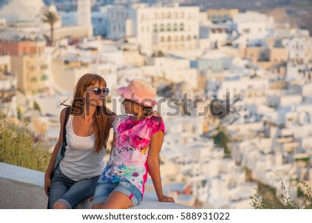 concept of family tourism and travel. Mom and daughter on a background of sunset city. Two girls tourists travel to the island of Santorini, Greece. Sunset on the most beautiful island 