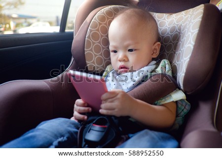 Cute asian toddler baby boy sitting in car seat and watching a video from smart phone. Kids playing in the car with smartphone. leisure & children & technology & internet addiction concept