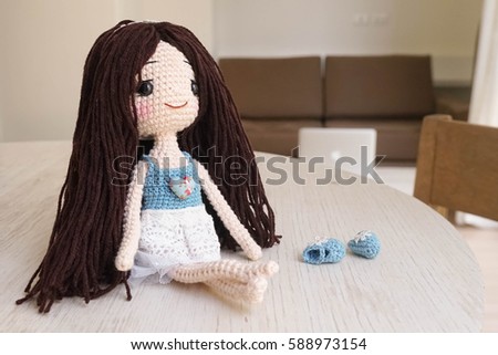 Crochet doll sitting by the window, with the abstract blur of metallic personal computer on the background. Vacation and relaxation concept