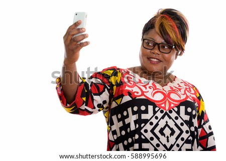 Studio shot of happy fat black African woman smiling while taking selfie picture with mobile phone and wearing eyeglasses