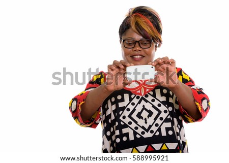 Studio shot of happy fat black African woman smiling while taking picture with mobile phone
