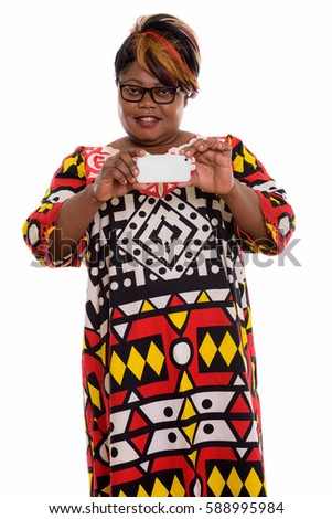 Studio shot of happy fat black African woman smiling and standing while taking picture with mobile phone