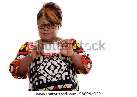 Studio shot of fat black African woman taking picture with mobile phone and looking at camera