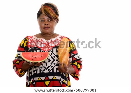 Studio shot of fat black African woman holding bread and slice of watermelon while thinking