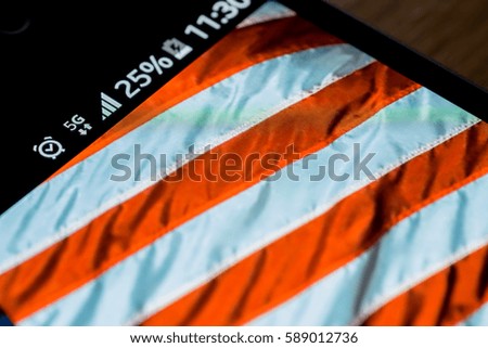 Smartphone on wooden background with 5G network sign 25 per cent charge and USA flag on the screen.