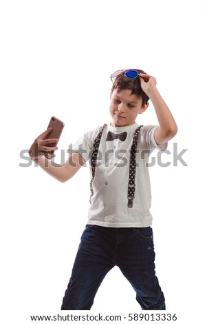Boy brunette in a white shirt with suspenders and sunglasses makes selfie phone on a white background