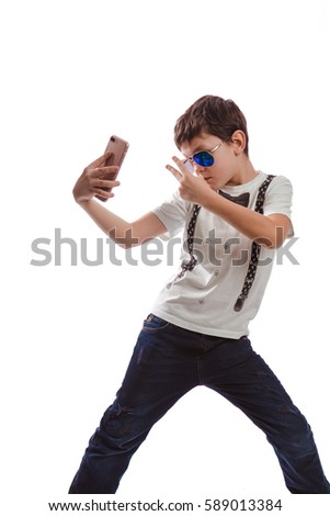 Boy brunette in a white shirt with suspenders and sunglasses makes selfie phone on a white background