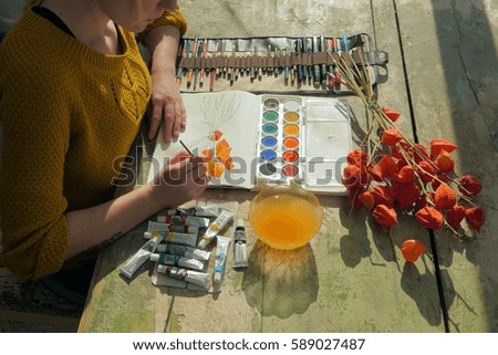 female artist painting a watercolor picture of a physalis plant into her notebook indoors, matching footage available in portfolio 