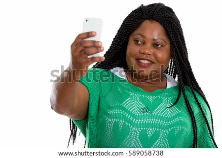 Studio shot of happy fat black African woman smiling while taking selfie picture with mobile phone