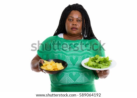 Studio shot of fat black African woman holding bowl of potato chips and lettuce served on white plate