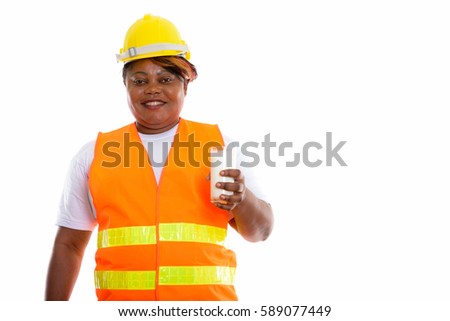 Studio shot of happy fat black African woman construction worker smiling while holding glass of milk