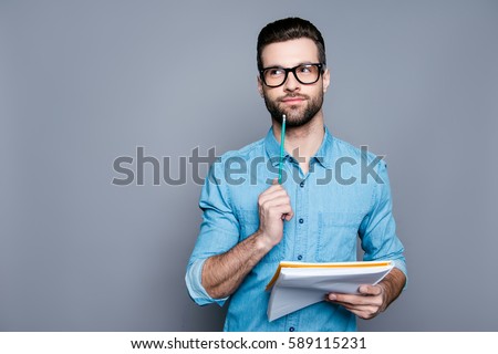 Young bearded guy in glasses holding a notebook and thinking about exams. Royalty-Free Stock Photo #589115231