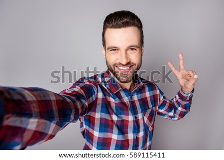 Young funny smiling man isolated on gray background taking a selfie and showing v-sing in camera.